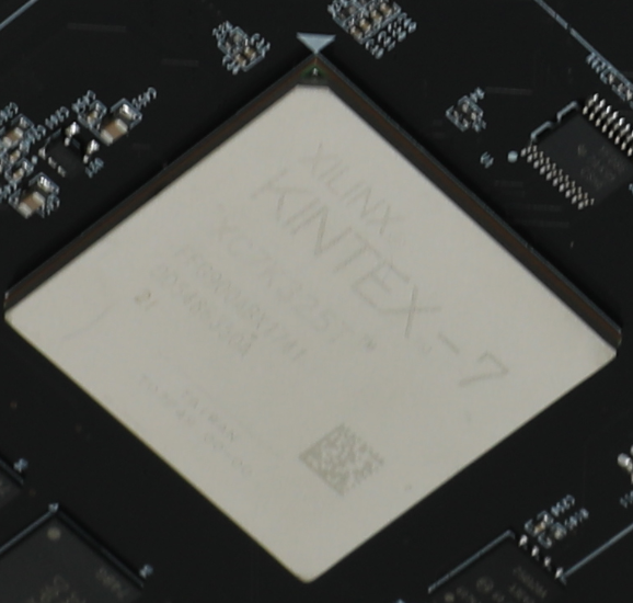 图片中展示了一块XILINX KINTEX-7 FPGA芯片，芯片上清晰地印有“XILINX KINTEX-7”字样，以及型号“XCAS25T-4”。芯片周围是电路板的其他部分，包括一些焊点和电路元件。图片在文档中用于展示FPGA芯片的实物，与上下文中的描述相呼应，帮助读者更好地理解FPGA芯片的外观和结构。