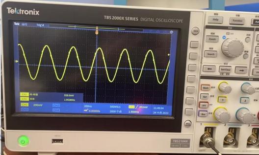 图片显示了一台Tektronix TBS2000X系列数字示波器的屏幕，屏幕上显示了一个正弦波形。屏幕左下角显示了波形的参数，包括100mV的垂直偏移和1.053ms的水平偏移。这表明示波器正在测试DAC输出的正弦波形。图片在上下文中用于展示使用SSMC转BNC的线连接到一路DAC输出到示波器后，可以在示波器上看到DA输出的正选波波形。