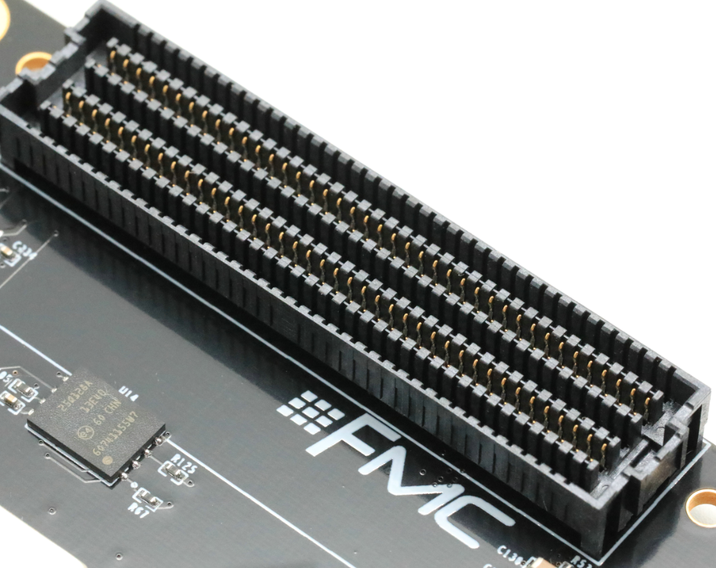 图片显示了AX7325B开发板上的FMC连接器实物图。连接器由多个黑色的针脚组成，排列整齐，针脚上标有金色的标识。连接器的左侧印有“FMC”字样，右侧则有电路板的部分电路元件。图片在上下文中起到直观展示FMC连接器实物的作用，帮助读者更好地理解FMC连接器的外观和布局。